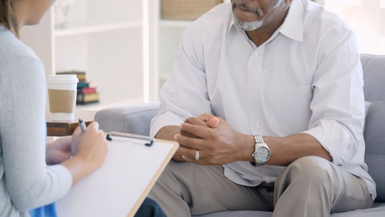 man sitting in a soft chair with his hands folded being interviewed by a female behavioral health therapist for sleep issues.